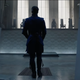 Doctor Strange, in handcuffs, approaches a seated, shadowed council in an antiseptic white room.